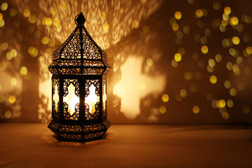 ornamental arabic lantern with burning candle glowing at night and glittering golden bokeh lights. f