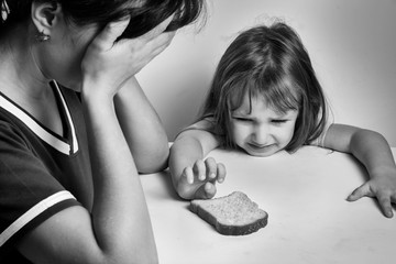 A depressed mother and a hungry daughter pulling her hand to a piece of bread. families with low incomes. crisis