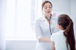 © zinkevych - Let me hear. Beautiful appealing female doctor hearing girl while using stethoscope and standing on light background