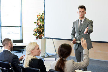 Portrait of handsome successful businessman answering questions from audience during training seminar