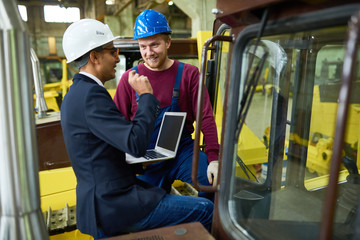 Portrait of industrial worker smiling happily while talking to supervisor using laptop, copy space