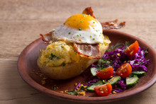 Baked Potato In Jacket Loaded With Cheese And Topped With Bacon And Fried Egg On Plate With Vegetables. Stuffed Potato With Topping