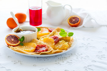 Wall Mural - French pancakes. Crepe Suzette with caramel, oranges, blueberries, almonds and hazelnuts on white table cloth