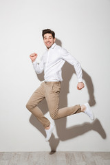 Sticker - Full length image ofcontent handsome man wearing stylish clothing, smiling and running along white wall with shadow