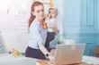 © Viacheslav Yakobchuk - Caring mother. Nice smart pleasant woman holding her daughter and looking after her while working on the laptop