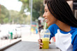 young african woman with braided hair sipping juice at cafe