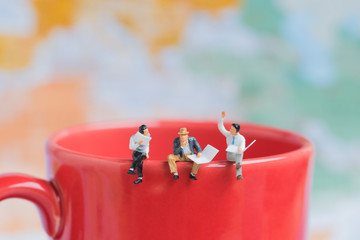 group of business miniature man sitting on red coffee cup edge with world map background