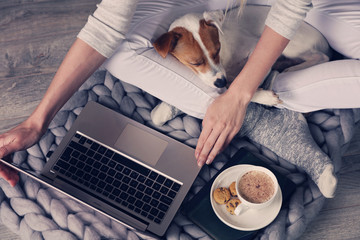 Woman in cozy home wear relaxing at home ,drinking cacao, using laptop. Soft, comfy lifestyle.