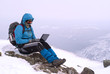 traveller working with a laptop in winter on top of a mountain during the snowstorm