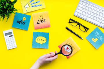 Poster - Social media promotion. Work desk with socail media icons. Yellow background top view. Hand with magnifier