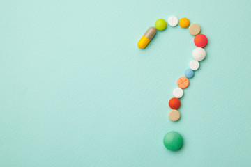 Symbol question mark from colored tablets and capsules on  green background. What medicines to choose better, what will help