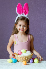 Wall Mural - A girl in a rim with rabbit ears, near a basket with eggs and colorful eggs