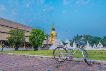 A bicycle of Buddha worshipper and the golden spire or pagoda of Wat Suan Dok in the background.