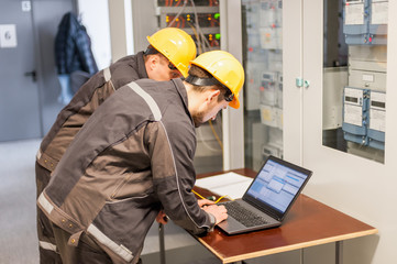 Wall Mural - two maintenance engineers inspect relay protection system with laptop comp
