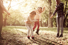 Cheerful Family Playing With Jump Rope Together In Park.