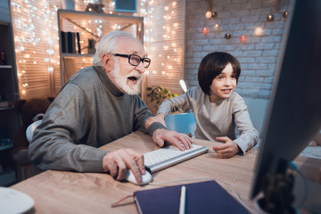 Grandfather and grandson are playing games on computer at night at home.