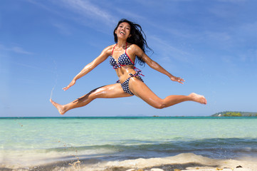 Wall Mural - A happy cheerful girl in the bikini jumping to the height on the sea beach. Active holidays on the tropical island. Beautiful asian woman runs in the transparent sea.