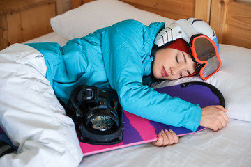 Canvas Print - Woman in sports clothes with snowboard sleeping on bed. Winter vacation