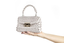 Woman's Hand Is Holding A Small Crocheted Cross Body Bag Of Beige Color Isolated On White Background.