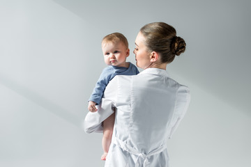 rear view of female pediatrician holding little baby on grey