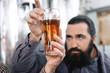 © freeograph - Bearded man looks at transparency of beer in glass. Brewer is studying density of beer in glass.