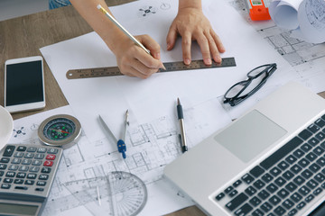 Top view, Architect or engineer hands working on blueprint plans with a pencil ,laptop a ruler, calculator, and engineering tools. Architect or engineer working on blueprint in office.