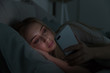 Portrait of young sleepy tired woman lying in bed under the blanket using smartphone at late night, can not sleep/ Insomnia, nomophobia, sleep disorder concept/ Dependency on a cell phone