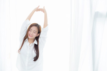 Wall Mural - Beautiful young asian woman stretch and relax standing in bed after wake up morning at bedroom, new day and resting for wellness, lifestyle concept.