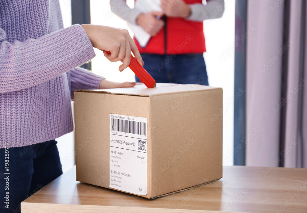 Young woman opening parcel at home, closeup