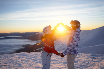 Canvas Print - Lovely couple holding hands in shape of heart on snowy peak at sunset. Winter vacation