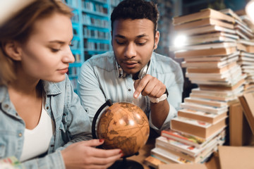 Wall Mural - Ethnic indian mixed race guy and white girl surrounded by books in library. Students are using globe.