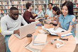 © freeograph - Six ethnic students, mixed race, indian, asian, african american and white surrounded with books at library.