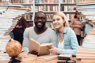 Wall Mural - Ethnic african american guy and white girl surrounded by books in library. Students are reading book.