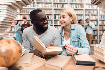 Wall Mural - Ethnic african american guy and white girl surrounded by books in library. Students are reading book.