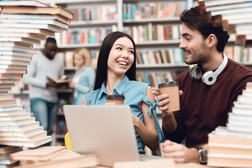 Wall Mural - Ethnic asian girl and white guy surrounded by books in library. Students are using laptop.