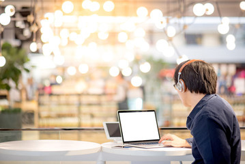 Young Asian business man listening to music by headphones while working with laptop computer in co working space. freelance or digital nomad lifestyle in urban workspace concepts