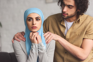 Wall Mural - muslim boyfriend hugging worried girlfriend in hijab in living room