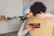 muslim girlfriend in hijab hugging boyfriend and holding present at home