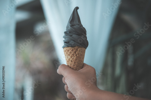 Fotografie, Obraz A hand holding charcoal soft serve ice cream cone with blur background