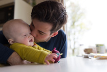 Young Father Kissing With Baby Boy At Breakfast Table
