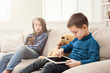 © Prostock-studio - Two kids with gadgets on couch at home