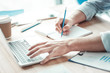 © zinkevych - Making notes. Competent worker keeping left hand on the keyboard and using pencil while writing results into copybook