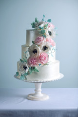 Beautiful three tiered white wedding cake decorated with flowers sugar pink peonies. Concept of elegant holiday desserts