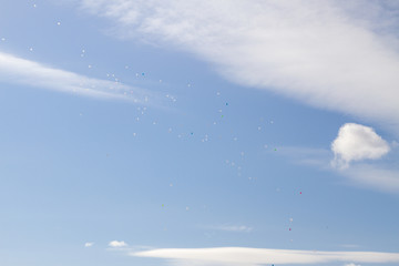 colorful balloons fly in the blue spring sky with white clouds