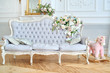 Sofa with gray upholstery, pillows and flowers on it, copy space. Luxury rich living room interior design with elegant classic furniture, rocking horse, mirror and candles. Vintage textile couch
