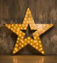Large Wooden Star With A Large Number Of Lights Are Lit. Beautiful Decor, Design. Loft Style Studio. Dark Concrete Background. Christmas, Holiday, Honorary Star. Five Stars 5 Stars