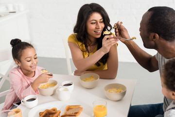 wife and husband feeding each other while having breakfast with kids