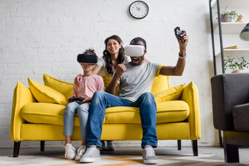 excited father and daughter playing video games while mother sitting behind and watching