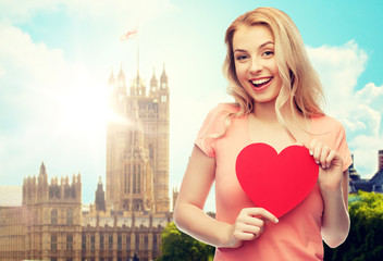 Canvas Print - love, travel, tourism, valentines day and people concept - smiling young woman or teenage girl with blank red heart shape over london city background