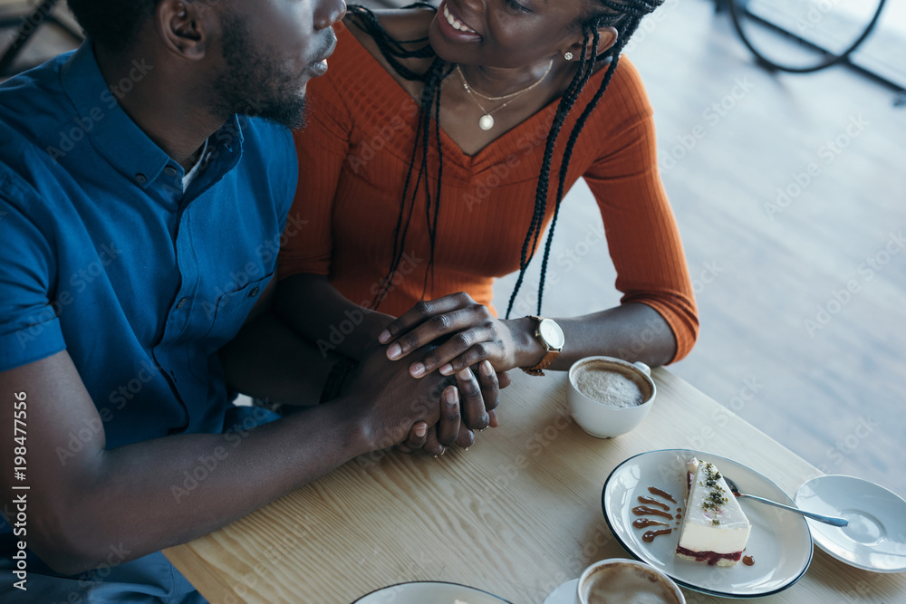partial view of african american couple holding hands while sitting at ...